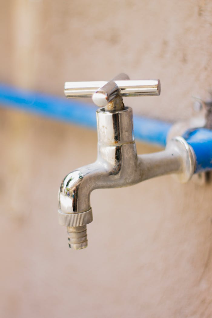 about-us A close-up view of a shiny stainless steel faucet attached to a blue pipe on a wall.